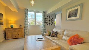 A living room with a sofa, a wooden coffee table, a lamp, a clock, and a framed picture on the wall.