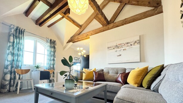 A living room with a grey sofa, a coffee table with a plant, a window with curtains, and a painting on the wall.