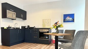 A modern kitchen with dark cabinetry, a built-in microwave, and a dining area with a table and two chairs.