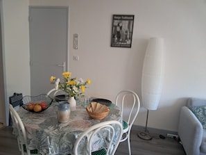 A dining area with a table set for two, a vase with flowers, and a wall-mounted picture.