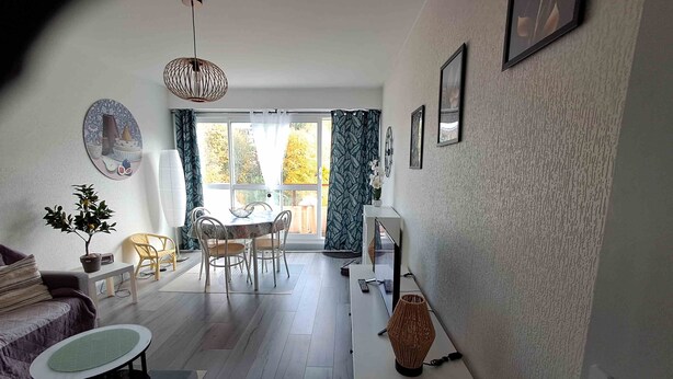 A modern living room with a dining area, a sofa, a small table, a lamp, and a TV on a cabinet.