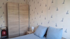 A bedroom with a bed, two pillows, a nightstand with a lamp, and a wardrobe.