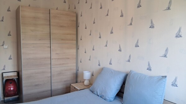 A bedroom with a bed, two pillows, a nightstand with a lamp, and a wardrobe.