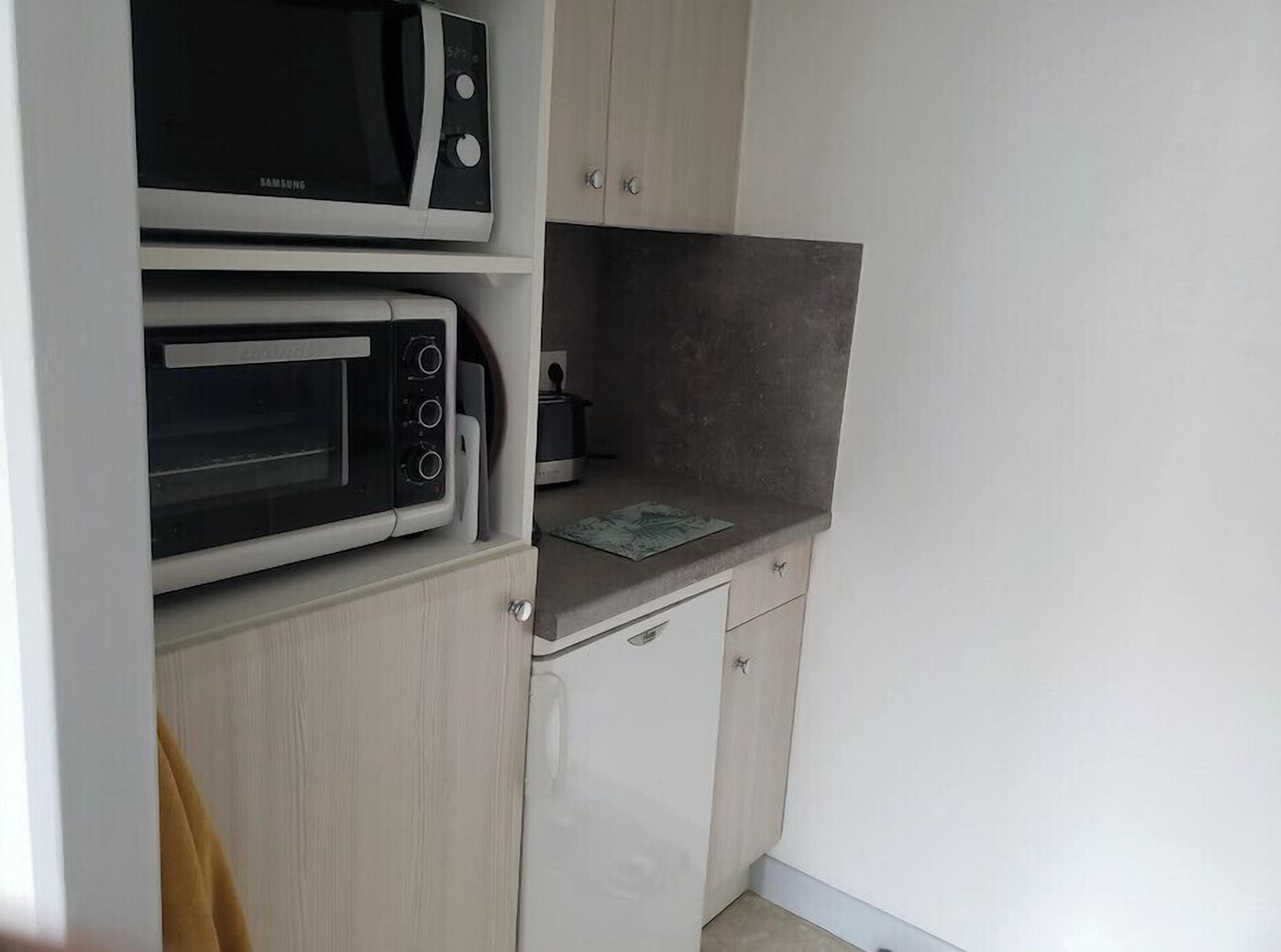 Une cuisine compacte équipée de deux micro-ondes fixés au mur, d’un petit plan de travail et d’un réfrigérateur blanc.