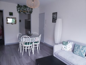 A living room with a dining area, white furniture, a black coffee table, and a large white lamp.