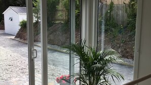 Een kamer met een grote schuifdeur die uitkomt op een tuin. Bij de deur staat een plant in een pot op een klein tafeltje.