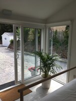 A room with a large sliding glass door leading to a garden area. There is a potted plant on a small table near the door.