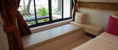 A bedroom with a large window, a built-in bench, a bedside table, and a bed with pillows.