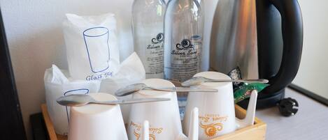 A tray with white mugs, two water bottles, a glass, and a kettle.
