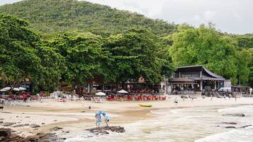 A beach with a restaurant and lounge area, surrounded by lush greenery.