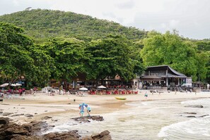 Una platja amb un restaurant i zona de relaxació, envoltada de vegetació abundant.