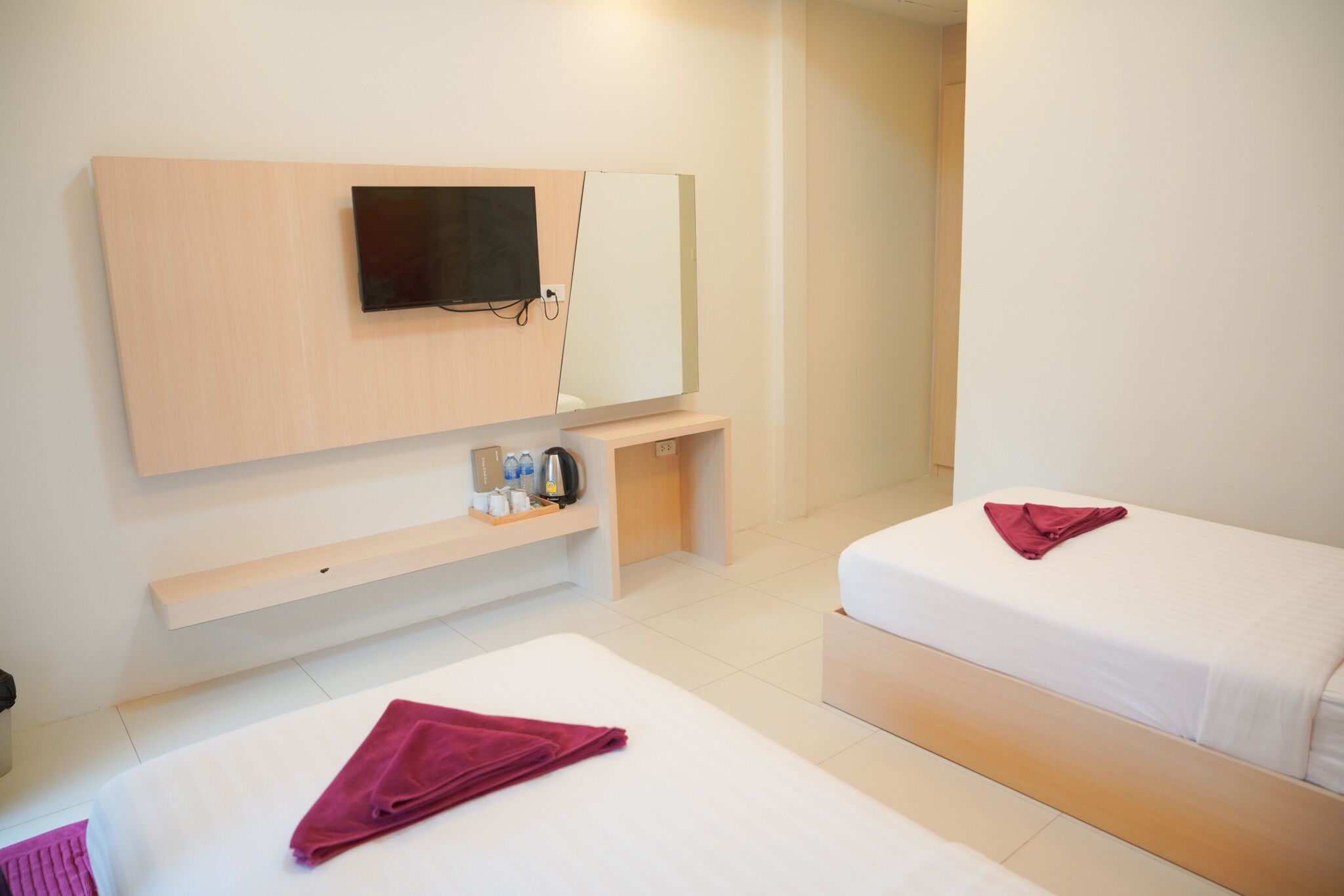 A hotel room with two beds, a TV mounted on the wall, a small shelf with toiletries, and a mirror.