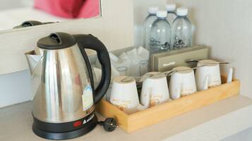 A kitchen area with a stainless steel kettle, a coffee maker, and a tray of disposable cups.