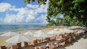 Un café situé en bord de mer, avec une terrasse ombragée par des parasols, offrant une vue sur l’océan.