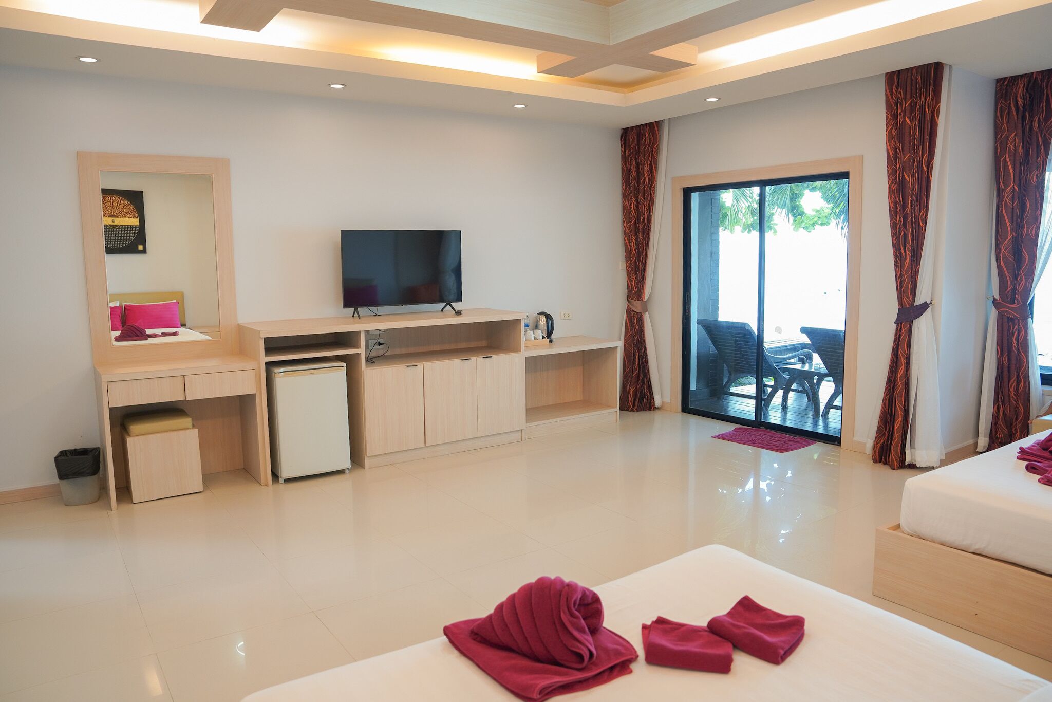 Een moderne hotelkamer met een flatscreen-tv, een bureau, een minibar, een bed met een rode handdoek en een schuifglazen deur naar buiten.