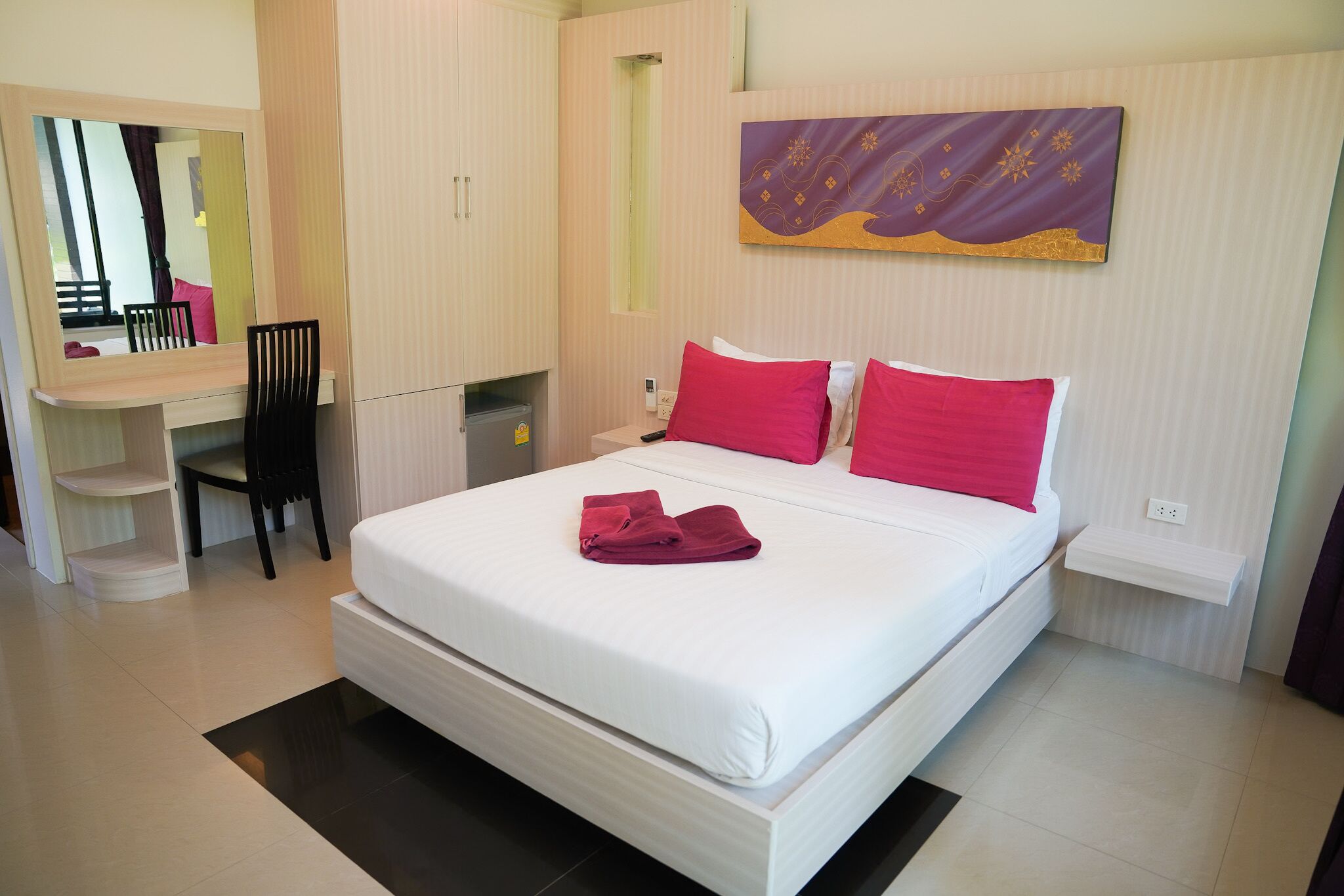 Ein Hotelzimmer mit Bett, Schreibtisch, Stuhl, Spiegel und einem an der Wand hängenden Kunstwerk.