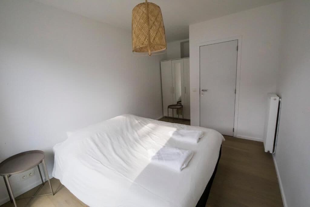 A bedroom with a bed, a small round table, a hanging light fixture, and a door.
