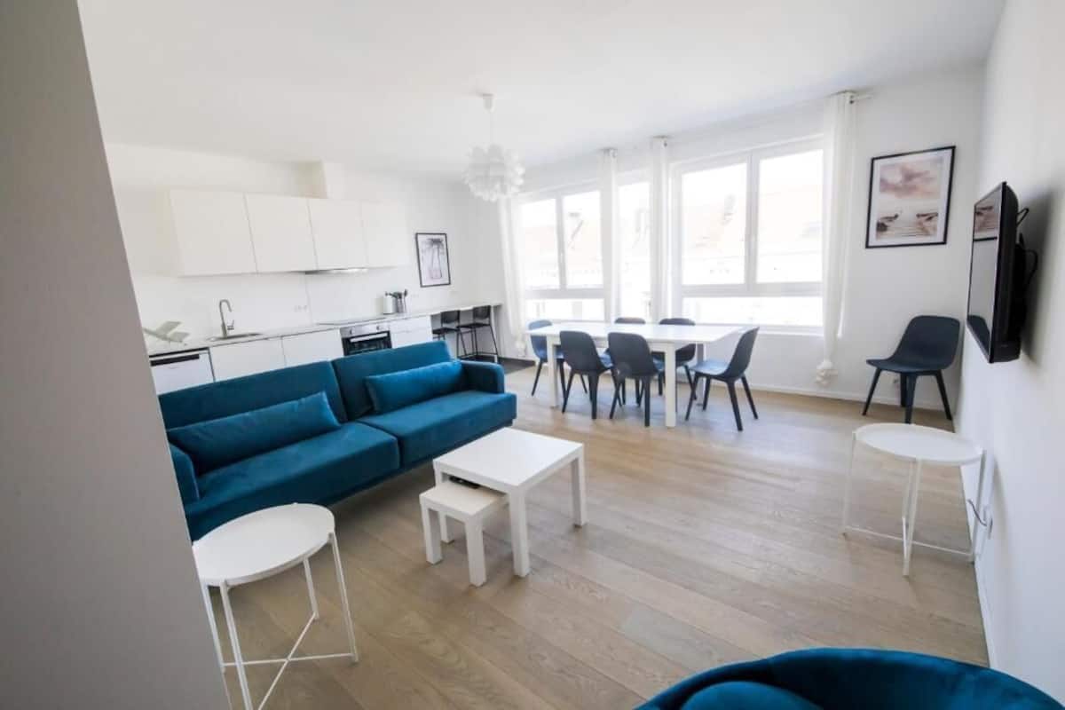 Ein modernes Wohnzimmer mit einem blauen Sofa, einem weißen Couchtisch und einem Essbereich mit Stühlen.
