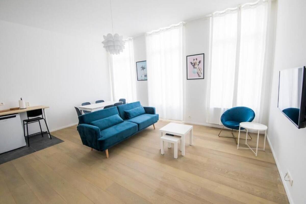 Ein modernes Wohnzimmer mit einem blauen Sofa, einem Esstisch und einer Küchenzeile.