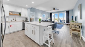 A modern kitchen with white cabinetry, a central island, and a dining area with a table and chairs. -  3rd floor 326 Newly Remodeled  Panama City Beach (Panama City Beach)