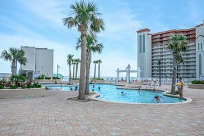 A pool area with palm trees, lounge chairs, and a large building in the background. -  3rd floor 326 Newly Remodeled  Panama City Beach (Panama City Beach)