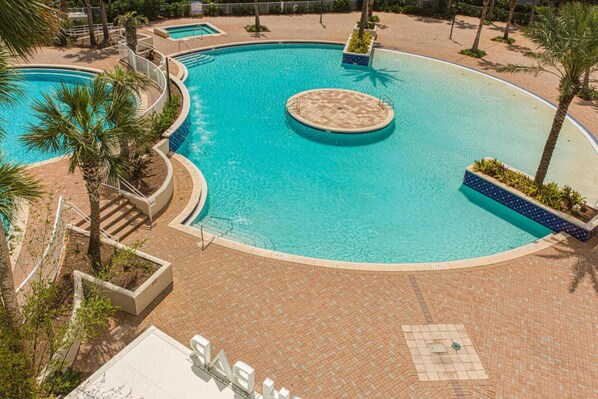 Una amplia piscina circular con una zona hundida en el centro, rodeada de palmeras y un solárium de ladrillo.