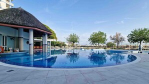 A swimming pool with a thatched roof structure, lounge chairs, and a clear sky.