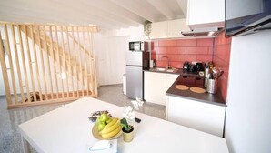 A modern kitchen with white cabinets, a red backsplash, and a wooden dining table with fruit and a vase. - Smart Appart Gare Du Midi (Brussels)