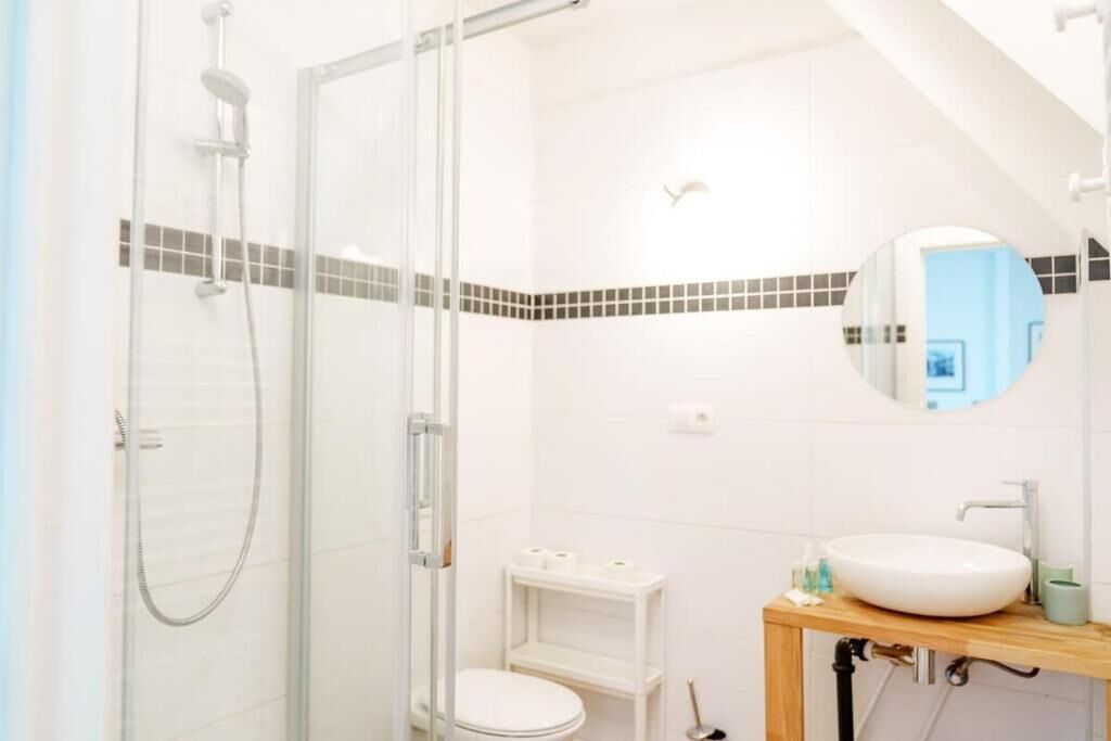 Een moderne badkamer met een douchecabine van glas, een wit toilet, een wastafel met spiegel en een klein plankje met toiletartikelen.
