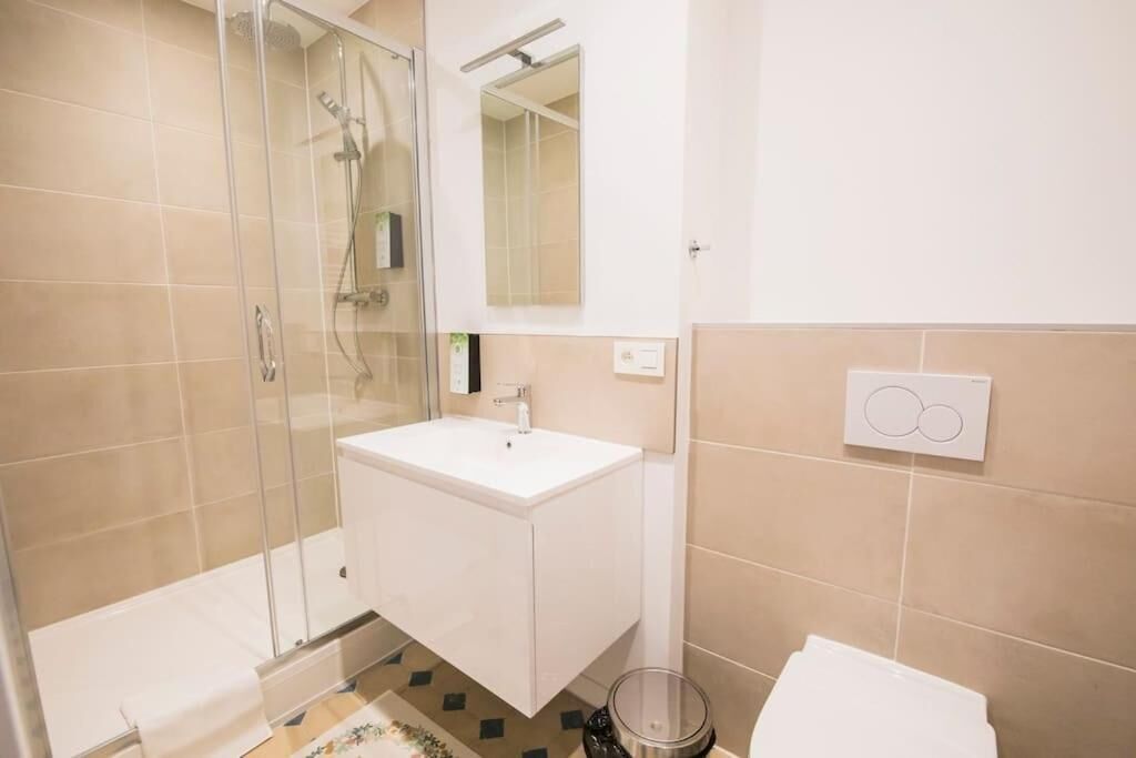 A bathroom with a glass shower enclosure, a white sink, and a toilet.
