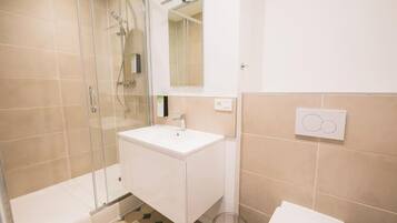 A bathroom with a glass shower enclosure, a white sink, and a toilet.