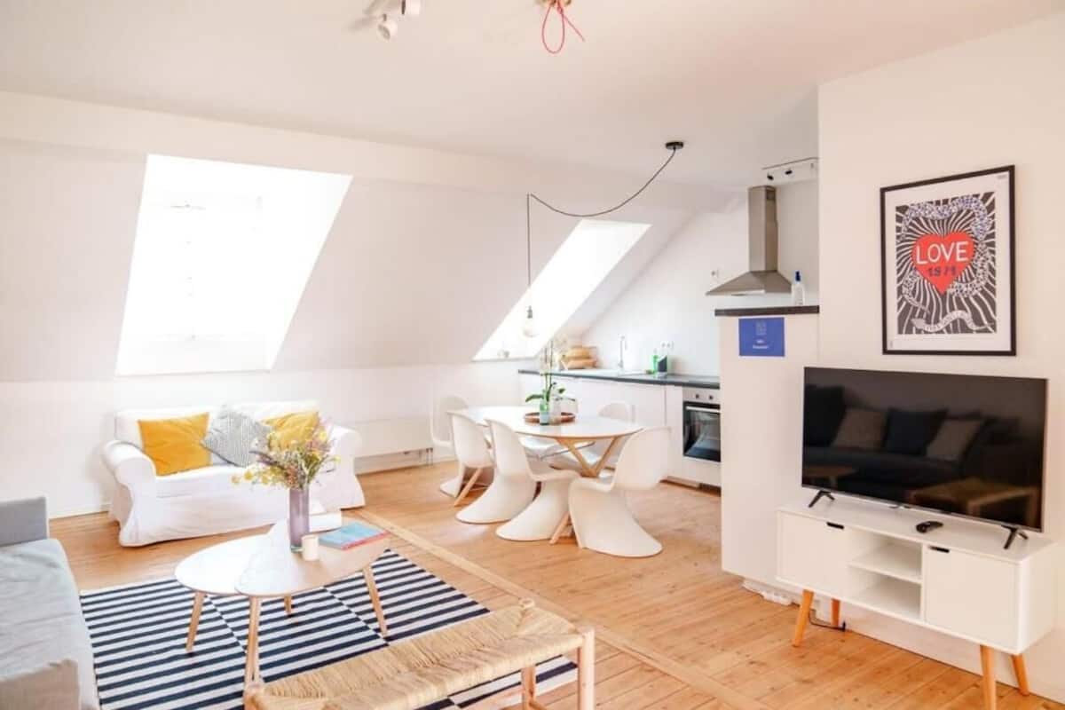 A modern living room with a white sofa, a dining table, and a TV.