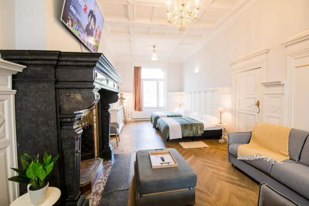 A hotel room with a fireplace, a sofa, a bed, and a television.