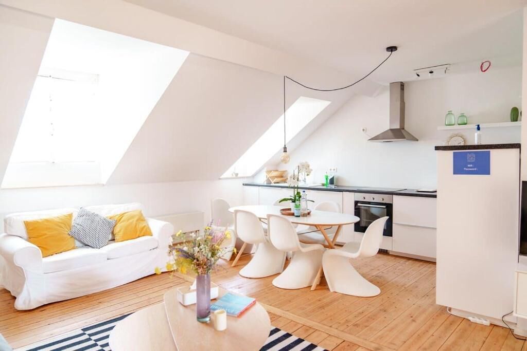 Un apartamento moderno con comedor, cocina y un sofá blanco con cojines amarillos.