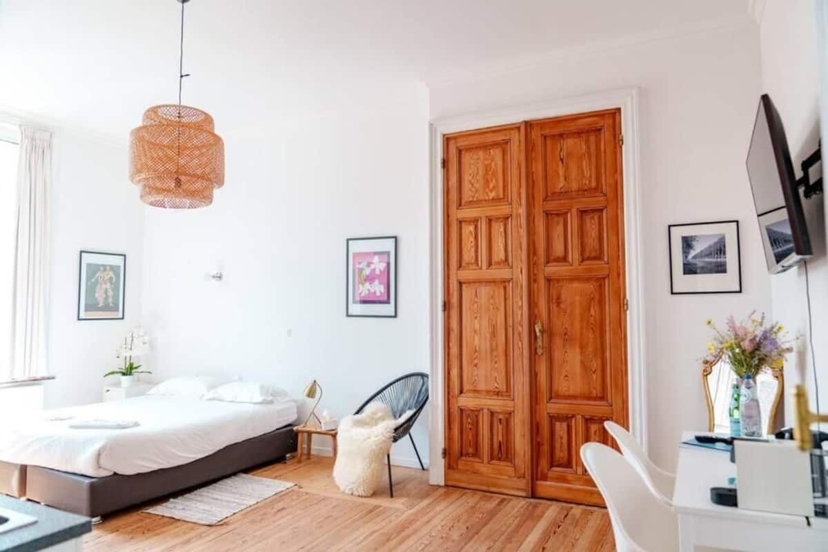 A bedroom with a bed, a chair, a desk, a wardrobe, and a hanging light fixture.