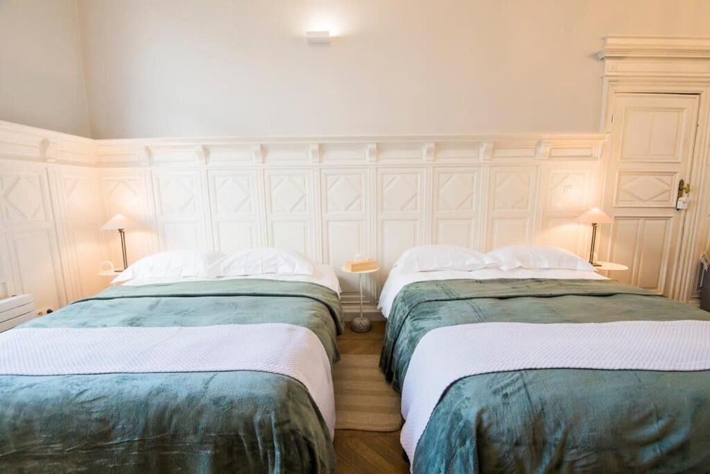 Una habitación de hotel con dos camas, un cabecero blanco y una mesita de noche pequeña con una lámpara.