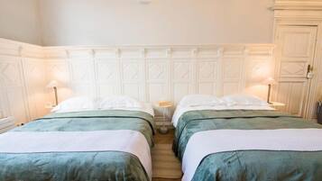 Una habitación de hotel con dos camas, un cabecero blanco y una mesita de noche pequeña con una lámpara.