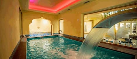 Una piscina interior con una fuente, suelo de baldosas y vistas al exterior.