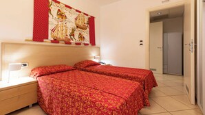 Habitación de hotel con dos camas, una mesita de noche, una lámpara de pared y una puerta que da a un armario.