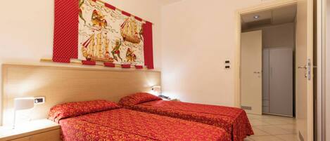 A hotel room with two beds, a nightstand, a wall-mounted lamp, and a door leading to a closet.