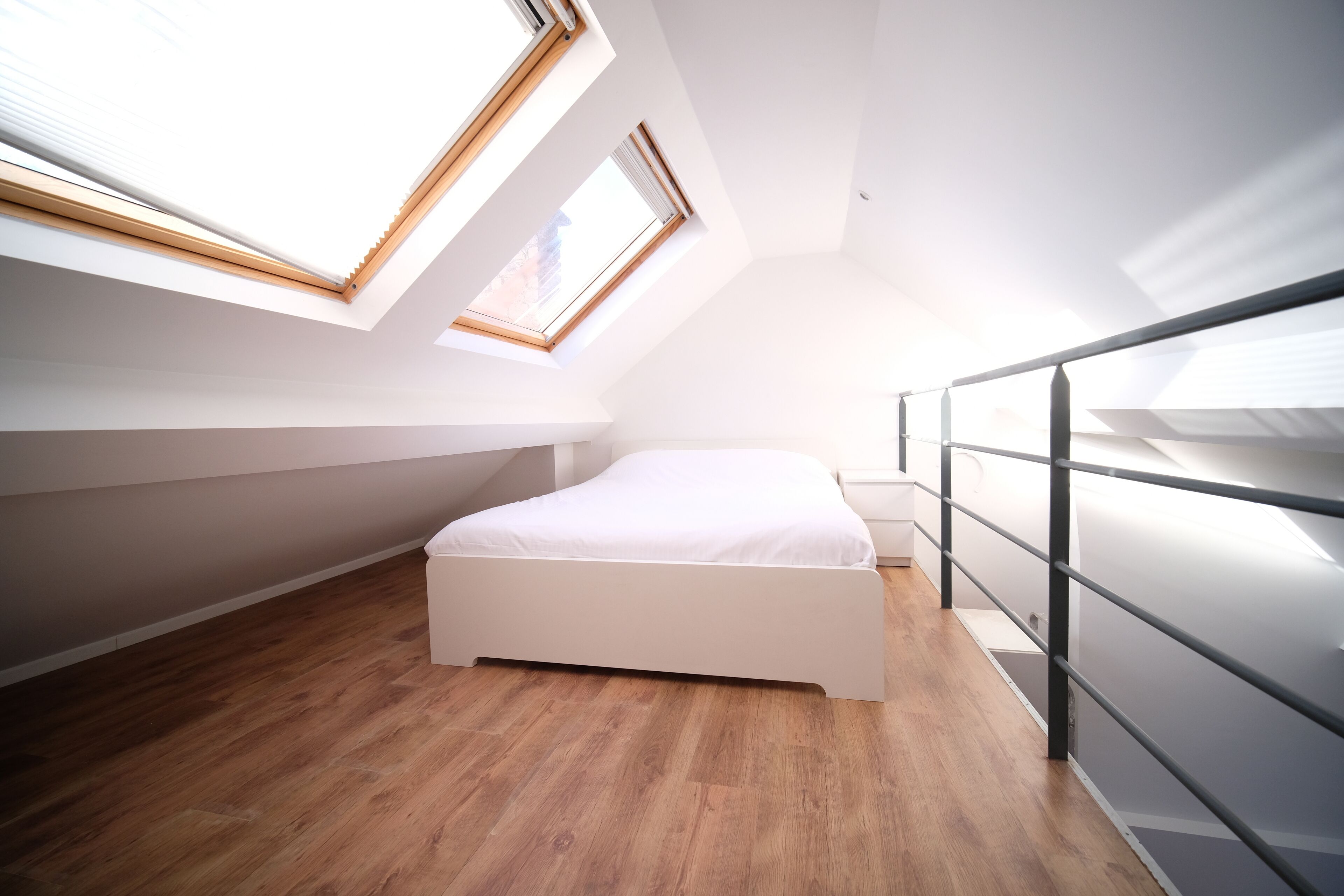 Une chambre moderne avec une lucarne, un plancher en bois et un lit blanc.