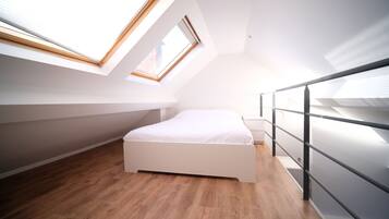 Une chambre moderne avec une lucarne, un plancher en bois et un lit blanc.