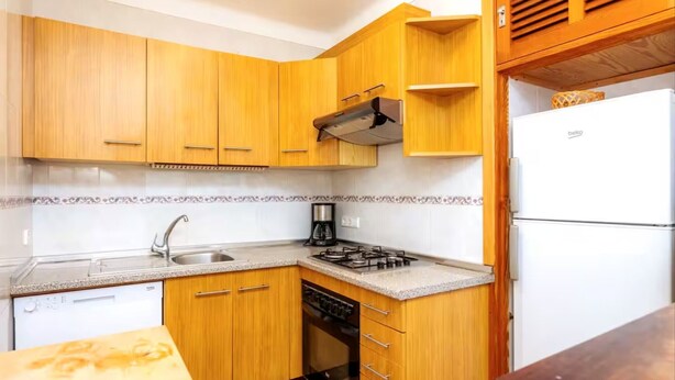 A compact kitchen with wooden cabinets, a gas stove, a built-in oven, a sink, and a refrigerator. - Casa Michaela, House 5StarsHome Mallorca. (Porto Petro)