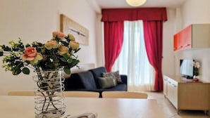 A living room with a sofa, a coffee table with a vase of flowers, and a dining area with a magazine.