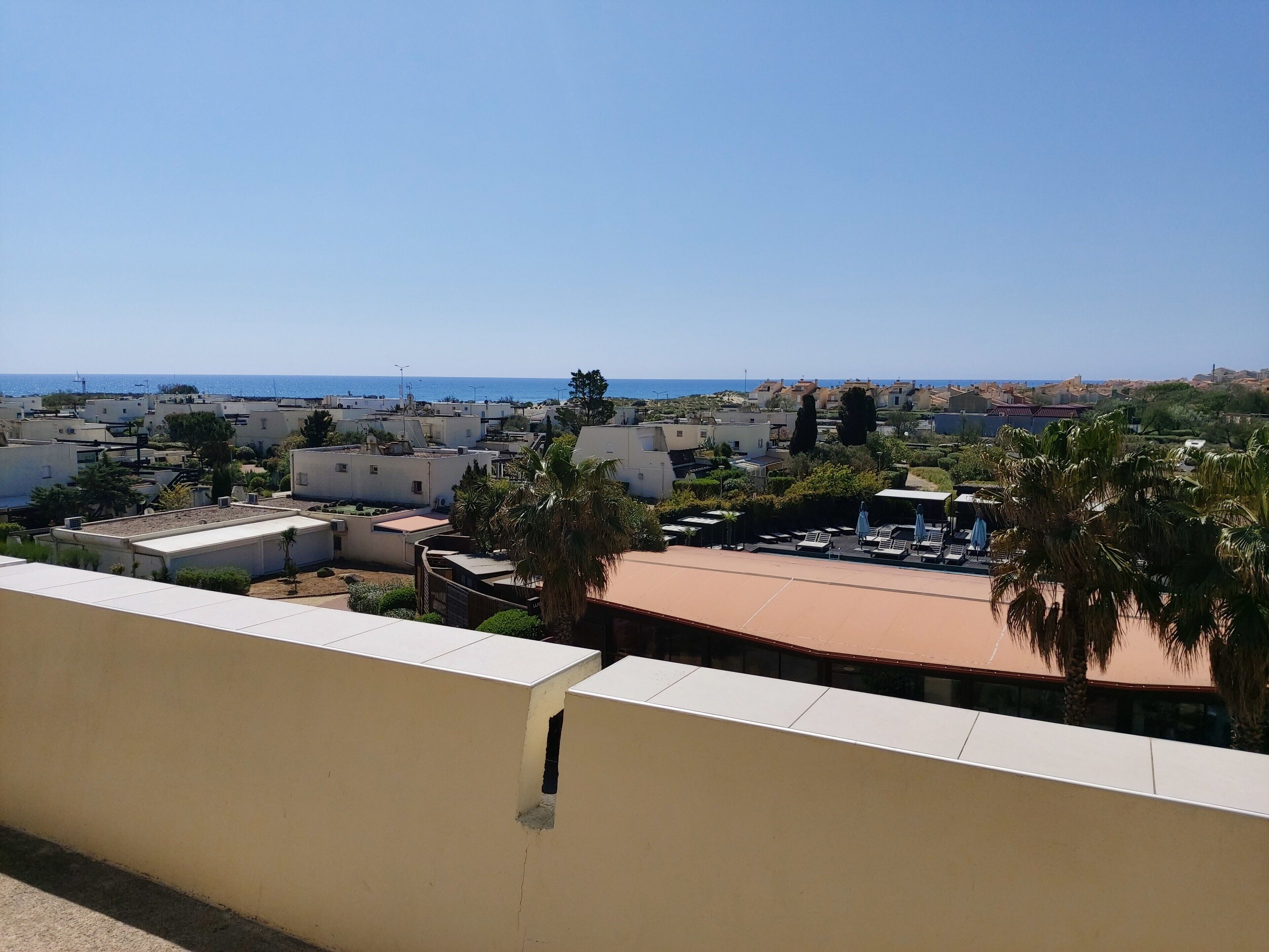 Ein Wohngebiet mit weißen Gebäuden, Blick auf das Meer und Palmen.