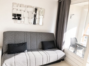 A modern living room with a patterned sofa, a geometric wall art piece, and a view of the outside through a window. - Naturiste Cap d'Agde Port Soleil 571 (Agde)