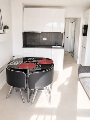 A modern kitchen with white cabinets, a black countertop, and a dining area with a round table and chairs. - Naturiste Cap d'Agde Port Soleil 571 (Agde)