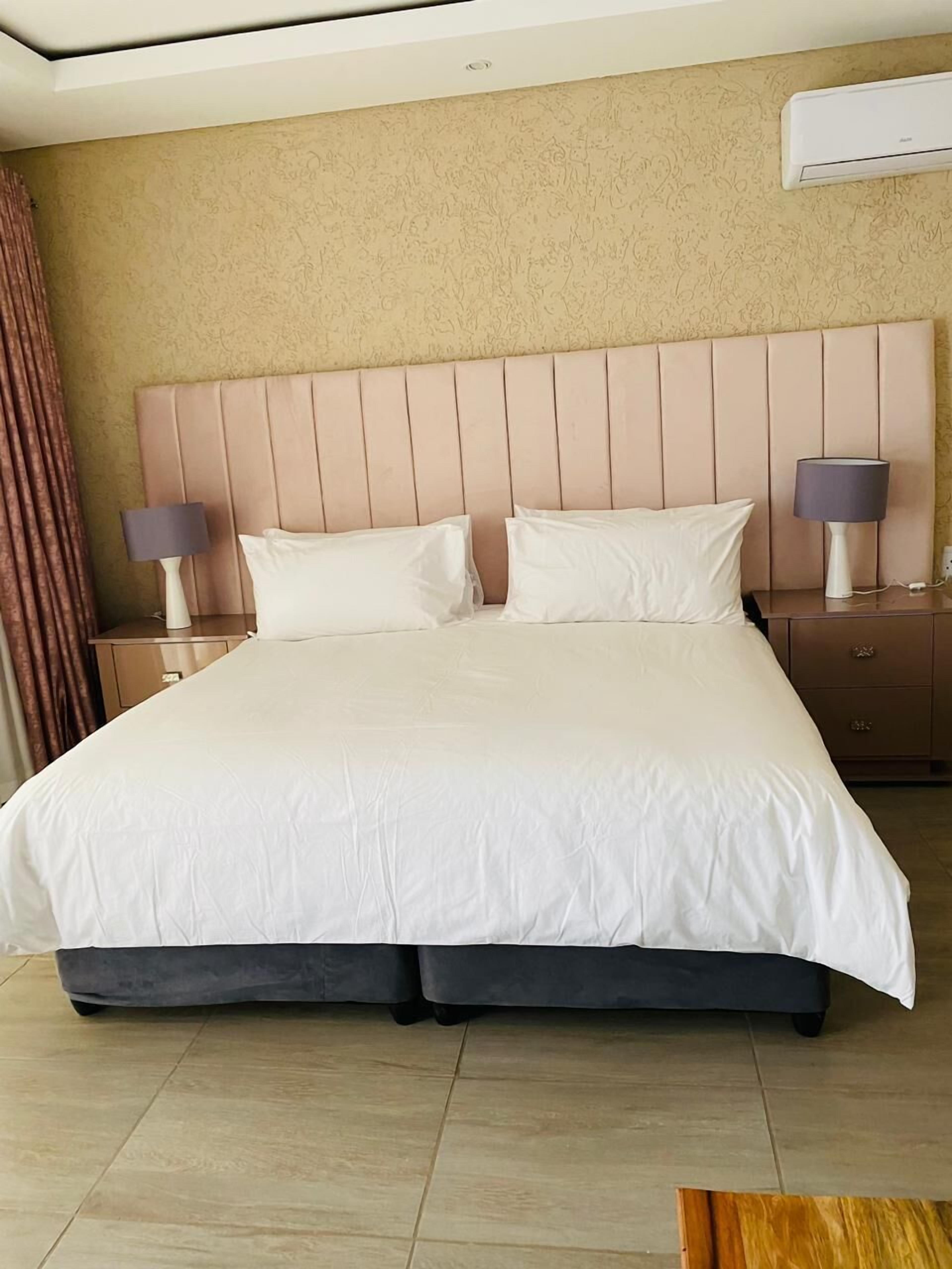 Habitación de hotel con una cama grande, dos mesitas de noche, aire acondicionado de pared y una cortina a la izquierda.