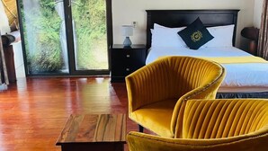 Una camera da letto con un letto, una sedia gialla, un tavolo in legno e vista su una cascata attraverso una porta vetrata.