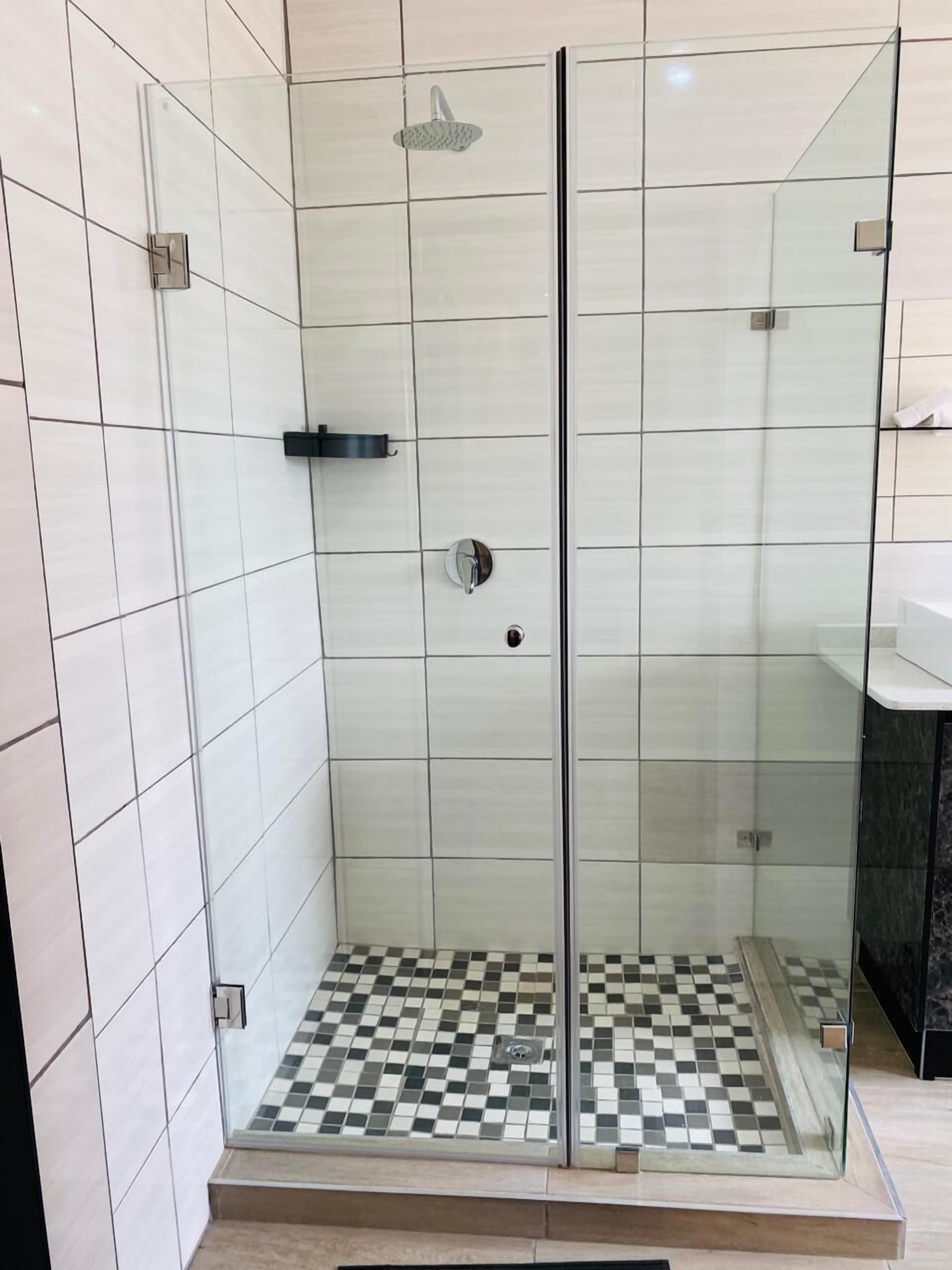 A glass-enclosed shower with a checkered floor, white tiles on the walls, and a black countertop to the right.